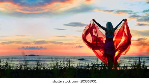 Young Woman With Hands Up Holding Red Scarf In Wind On The Beach