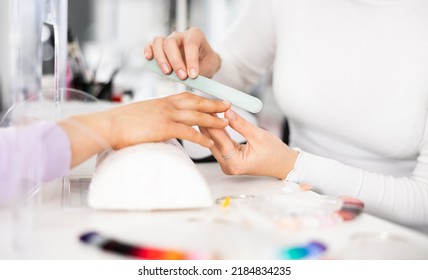 Young woman hands in a nail salon, which the manicure master files the nails with a nail file, giving them shape