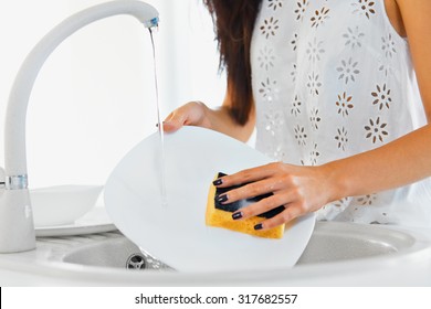 Young woman hands with nice manicure washing dishes in the sink in the kitchen using sponge with soap foam . Close up view.