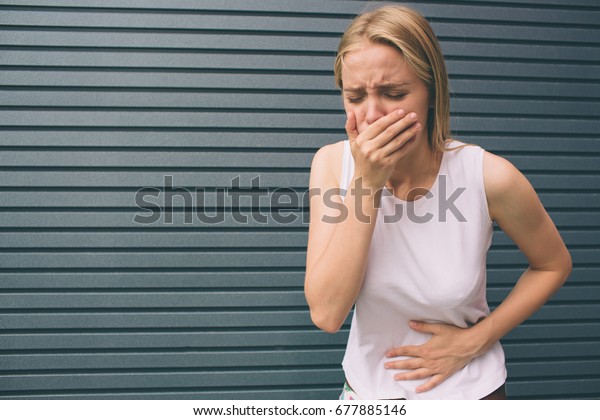 Young woman with hands on stomach having\
bad aches pain isolated on gray background. Food poisoning,\
influenza, cramps. Health issues problems\
concept