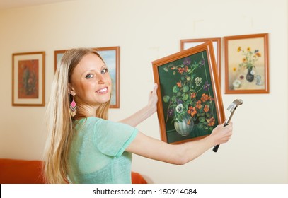 Young Woman Hanging The Art Picture On Wall At Home