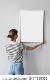 Young woman hanging an artwork, blank empty frame mockup