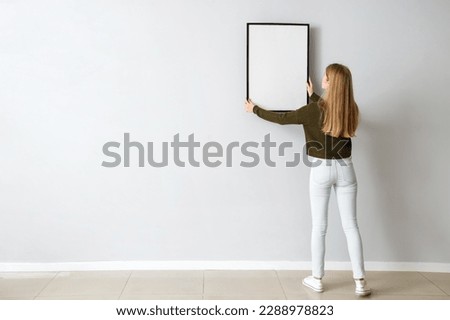 Young woman hanging blank frame on light wall at home, back view ストックフォト © 