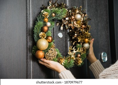 Young Woman Hanging Christmas Festive Wreath On House Door. Traditional Home Decoration On Winter Holidays, Female Hands Closeup Holding Fir Tree Handmade Wreath On Doorway.