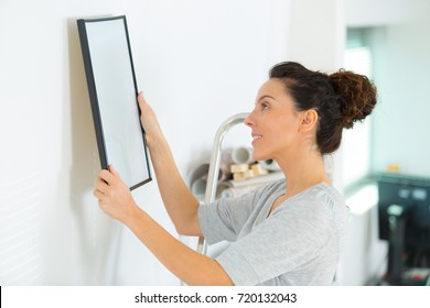 Young Woman Hanging A Picture On The Wall