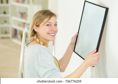 Young Woman Hanging A Picture On The Wall