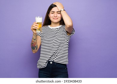 Young woman with a hangover holding a beer. Good-looking hispanic woman with a headache rubbing her head because of the alcohol