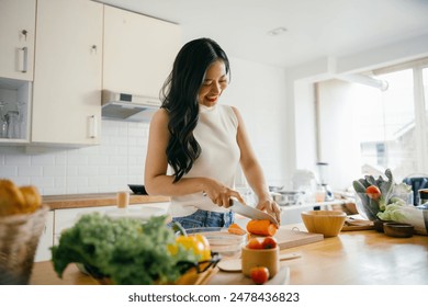 A young woman happily chopping vegetables in a bright, modern kitchen with natural light streaming through the windows. - Powered by Shutterstock