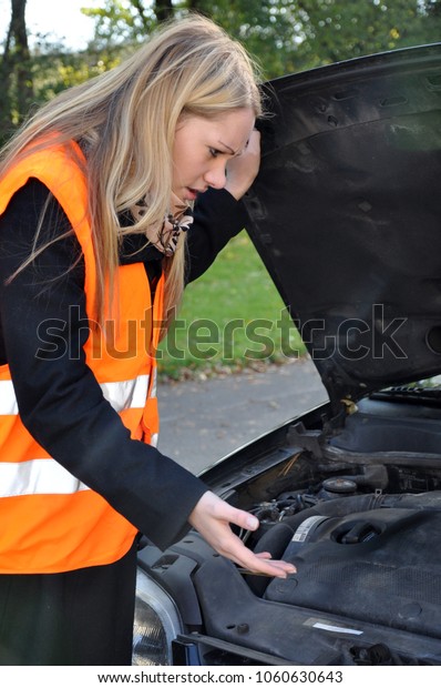Young woman has a breakdown with her car and wears\
safety vest