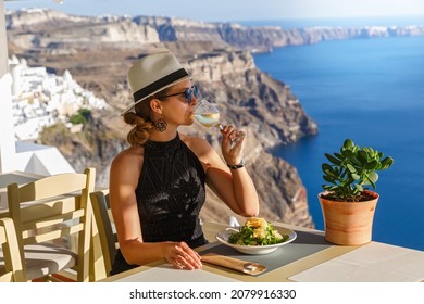 Young woman has breakfast in a restaurant overlooking the sea and the island of Santorini, Greece