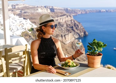 Young woman has dinner in a restaurant overlooking the sea and the island of Santorini, Greece