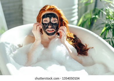 Young Woman Has Unpleasant Side Effect From Testing New Cosmetological Facial Mask While Taking A Bath . Woman Is Frightened Or Unpleasantly Surprised Feeling Pain, Burn And Discomfort.