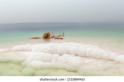 Young Woman With Hat Floating In The Waters Of The Dead Sea 