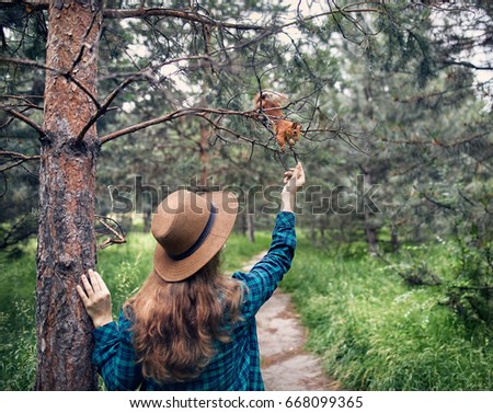 Young woman in hat with long hair feeding funny squirrel in pine forest