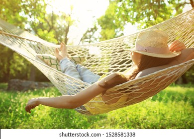 Молодая женщина в шляпе отдыхает в удобном гамаке в зеленом саду