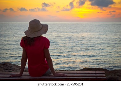 Young woman in hat sitting and looking at sunset 