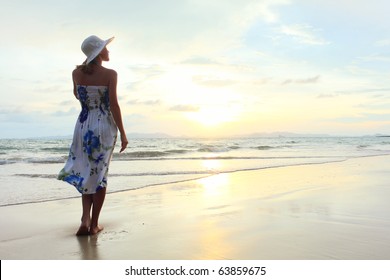 Young woman in hat standing on sand and looking to a sky