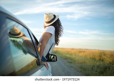 Young woman with hat sticking her body out of a car window. Freedom and adventure concept.