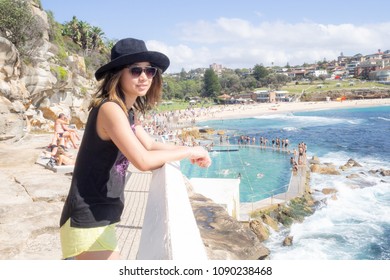 Young Woman With Hat And Sunglasses Walking By The Public Swimming Pool At Bronte Beach In Sydney Australia