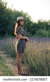 Young woman in hat walks on pathway along lavender field.