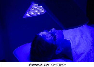 Young woman having blue LED light facial therapy treatment in beauty salon. Beauty and wellness concept