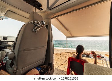 A young woman having breakfast in her caravan observing a good view of the beach
