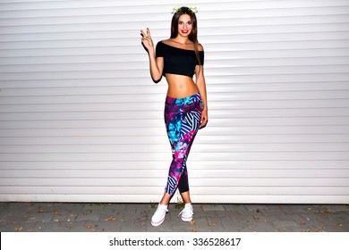 Young woman having fun, fit sexy body, wearing printer sport legging crop top, long brunette hairs, bright make up, urban wall background.