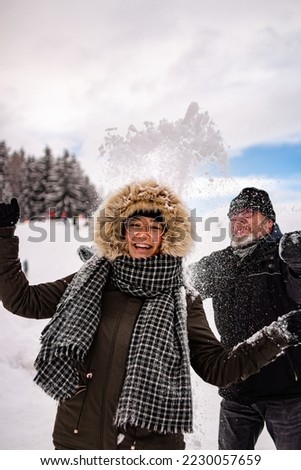 young woman having fun in the snow smiling as snow is thrown towards her by her father; recreational active winter concept;	