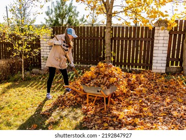 Young Woman having fun throwing while cleaning fallen maple autumn leaves in the garden.