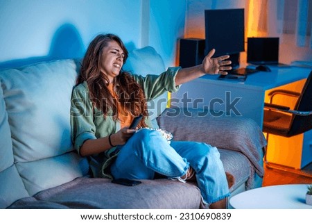 Young woman having fun watching TV at home late at night, annoyed and angry yelling at TV
