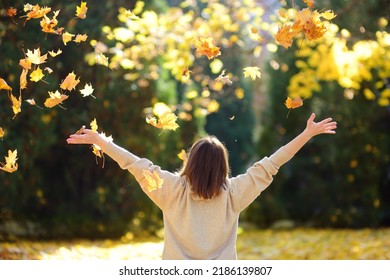 Young woman is having fun while walking through the forest on a sunny autumn day. Girl plays with maple leaves and throws them up. Fallen leaves rustle.