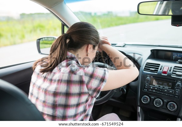 Young woman having headache, has to make a stop\
after driving car in traffic jam on rush hour. Exhausted,\
overworked driver concept