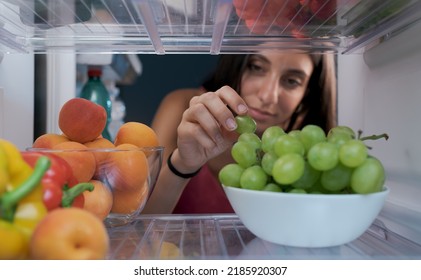 Young Woman Having A Healthy Snack, She Is Taking Fruit In The Fridge, POV Shot From Inside Of The Fridge