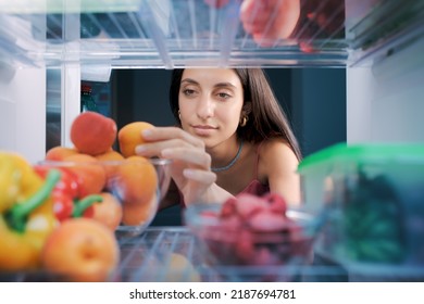 Young Woman Having A Healthy Snack, She Is Taking Fruit In The Fridge, POV Shot From Inside Of The Fridge