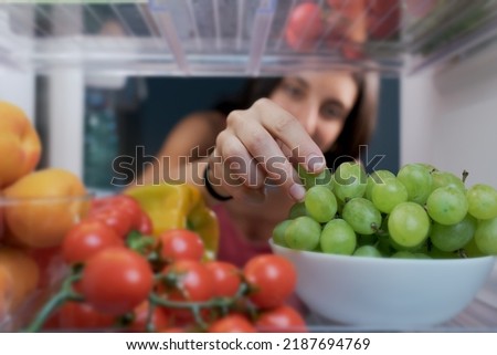 Young woman having a healthy snack, she is taking fruit in the fridge, POV shot from inside of the fridge