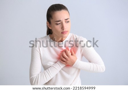 Young woman having heart attack on light background