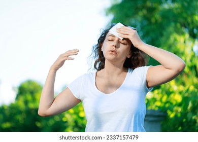 Young woman having hot flash and sweating in a warm summer day. Woman drying with paper napkin in too hot weather - Powered by Shutterstock