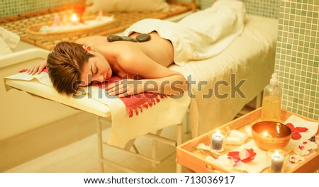 Young woman having hot stone therapy massage in spa hotel resort - Female enjoying package holiday special treatment - Body care, wellness and relaxing concept - Focus her eye - Warm filter
