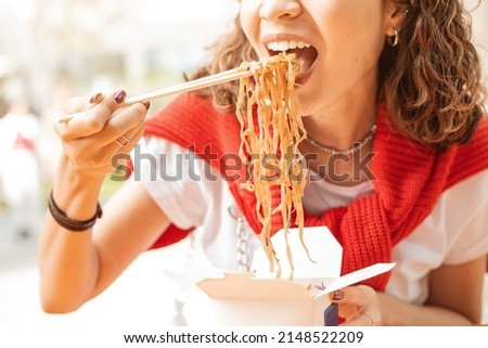 Young woman having a lunch break and eating wok noodles outdoors. Fastfood meal concept