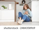 Young woman having panic attack on floor in kitchen