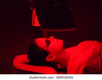 Young woman having red LED light facial therapy treatment in beauty salon. Beauty and wellness concept