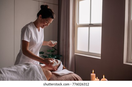 Young woman having spa procedure on her face. Woman lying on spa table and cosmetologist applying cosmetic mask on the her face in sap salon.