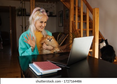 Young woman having video call via computer in the home office. Colorful  woman working on laptop at home small dog and cat besides Stay at home and work from home concept during Coronavirus pandemic. 