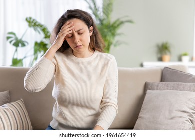 Young woman with headache sitting on sofa. General health problems concept - migraine. 