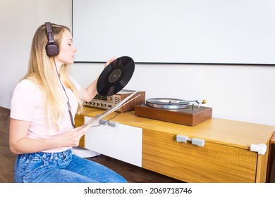 Young Woman With Headphones Listens To Music From Vinyl Records On A Turntable At Home.