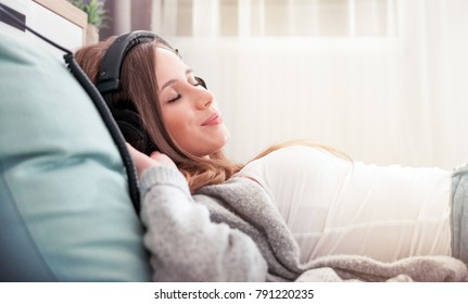 Young woman with headphones lying on floor listening to music at home in living room