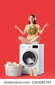 Young woman in headphones meditating on washing machine against red background - Shutterstock ID 2365082793