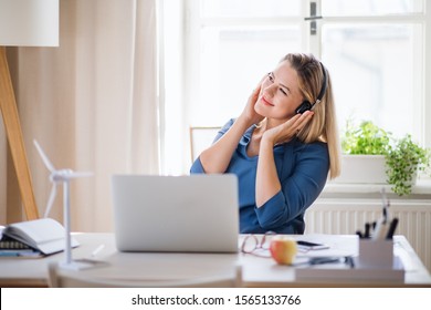 Young Woman With Headphones Sitting At The Desk Indoors In Home Office.