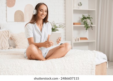 Young woman in headphones using tablet computer on bed at home - Powered by Shutterstock