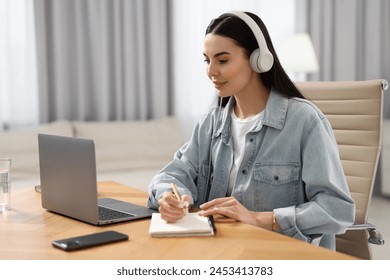 Young woman in headphones watching webinar at table in room - Powered by Shutterstock